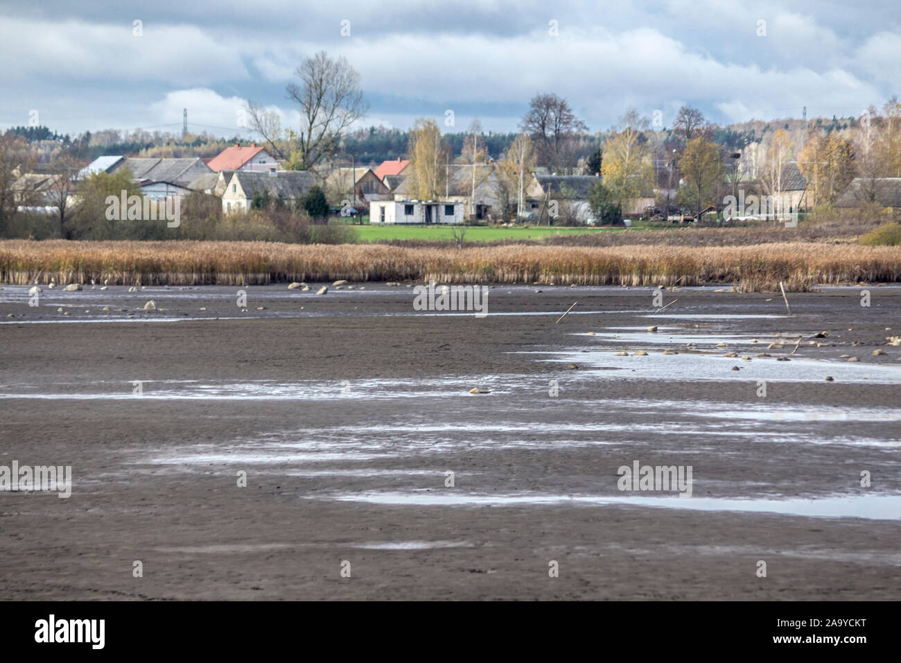 A pond for breeding fish without water. The dry bottom is covered with cracks. The village in the background. Fishing industry. Podlasie, Poland. Stock Photo