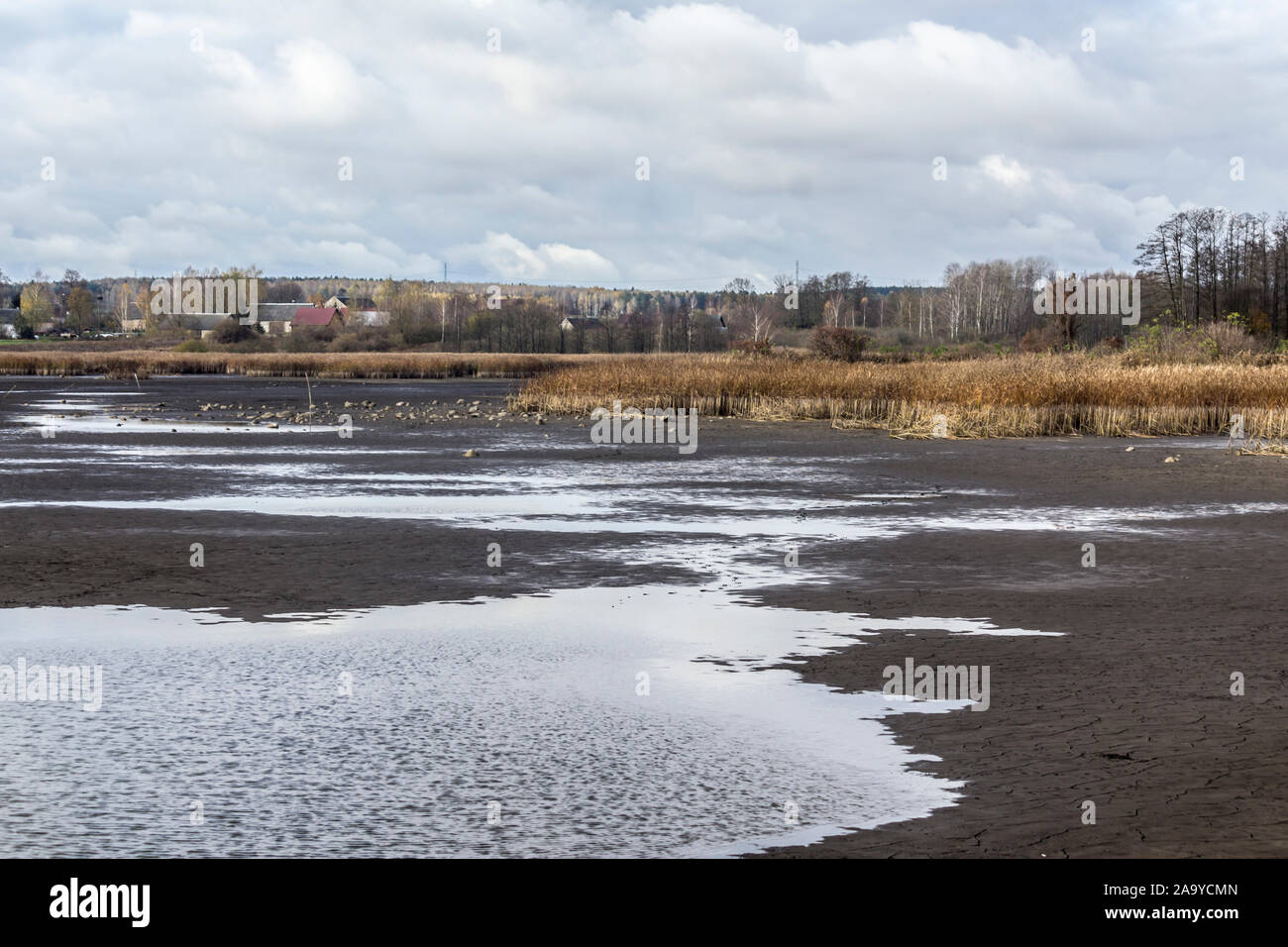 Pond for breeding fish without water.The dry bottom is covered with cracks and stones.The village in the background.Fishing industry.Podlasie, Poland. Stock Photo