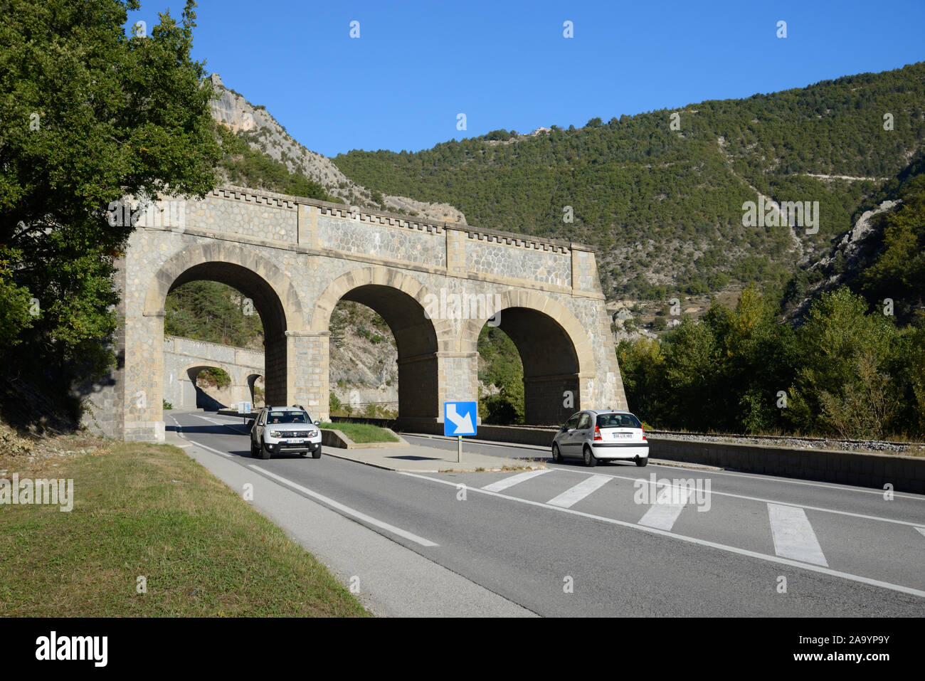 Cars Drive Under a Rock Shed, Water Channel Overbridge or Aqueduct Designed to Channel River Water & Overspill over Road to Prevent Flooding France Stock Photo