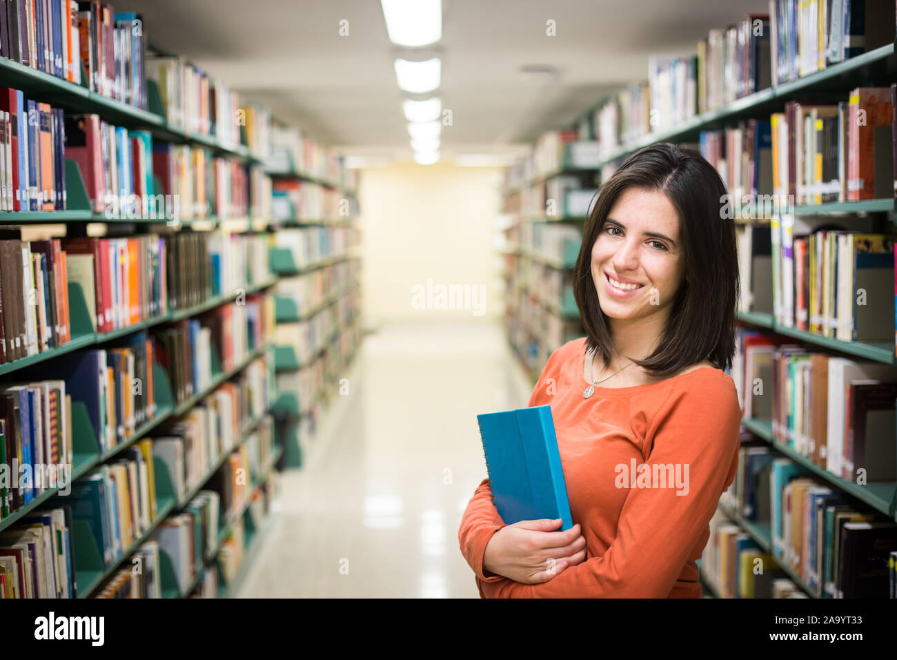 In the library - pretty female student with books working in a high school library. Stock Photo
