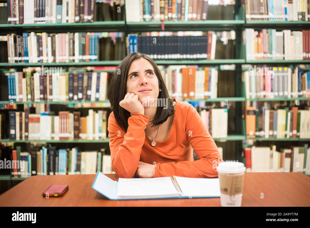In the library - pretty female student thinking working in a high school library. Stock Photo