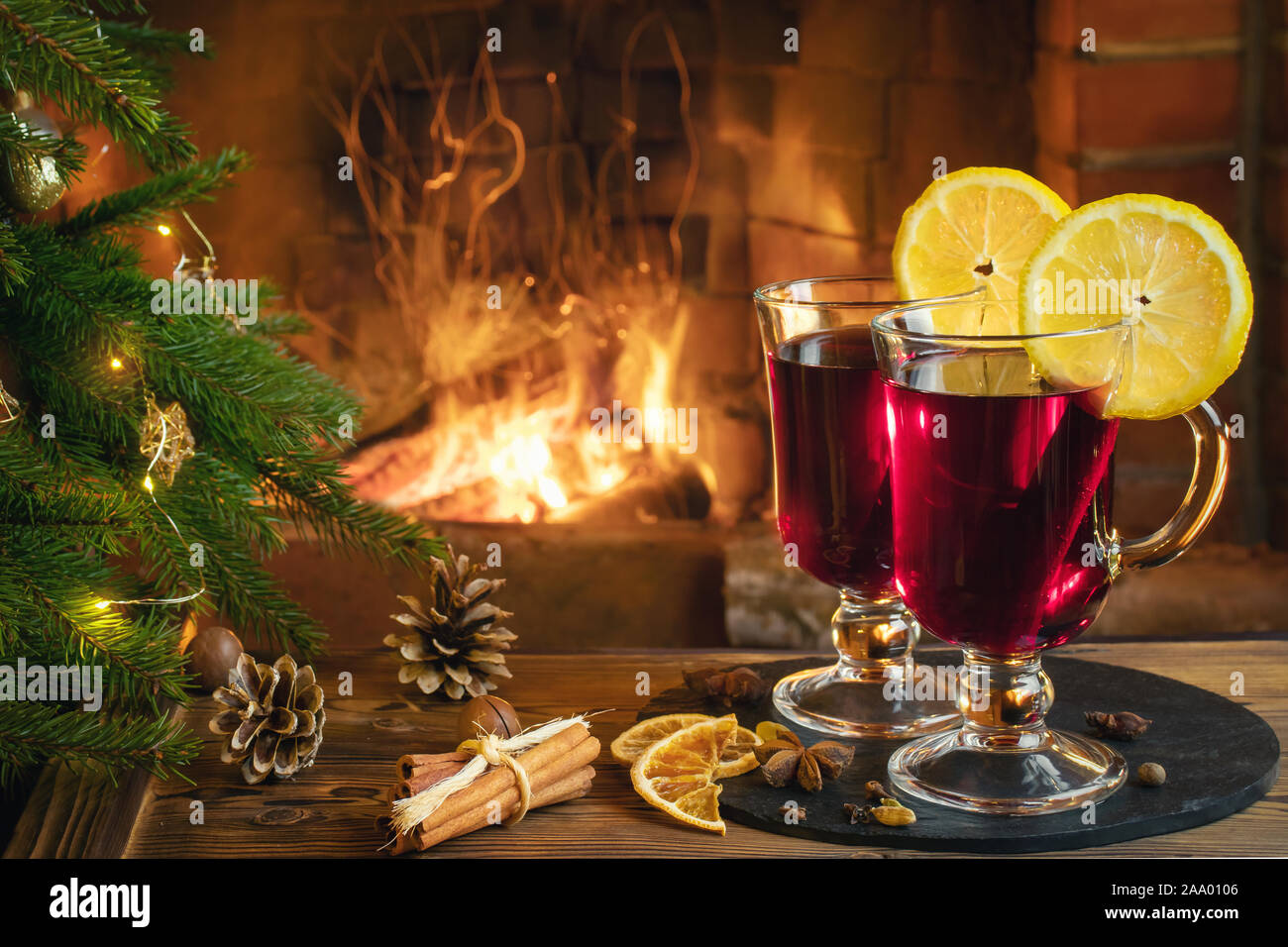 Christmas composition - two glasses with mulled wine on a wooden table near  a Christmas tree opposite a burning fireplace Stock Photo - Alamy