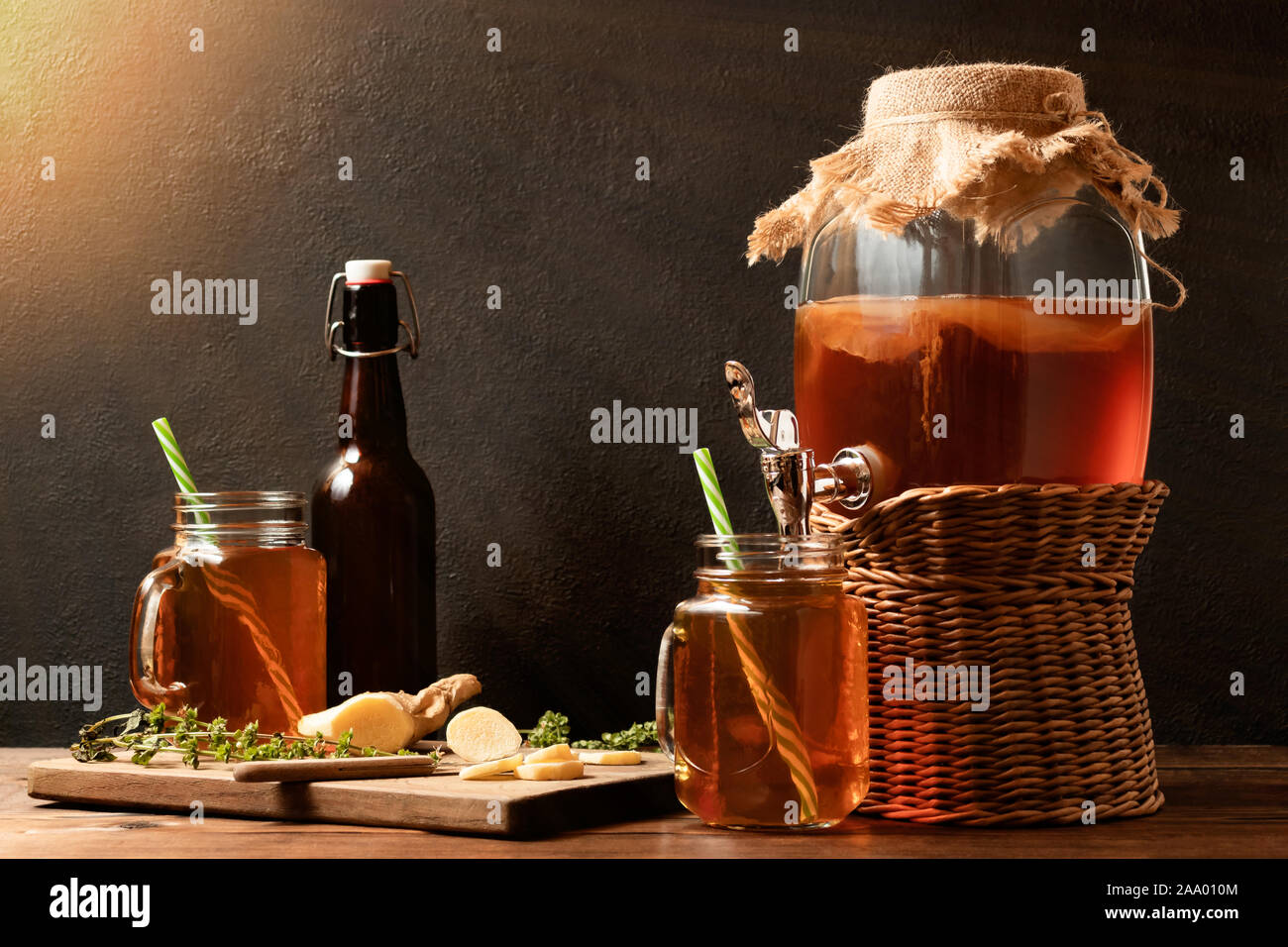 Fresh homemade Kombucha fermented tea drink in jar with faucet and in cans-mugs and bottle on black background. Stock Photo