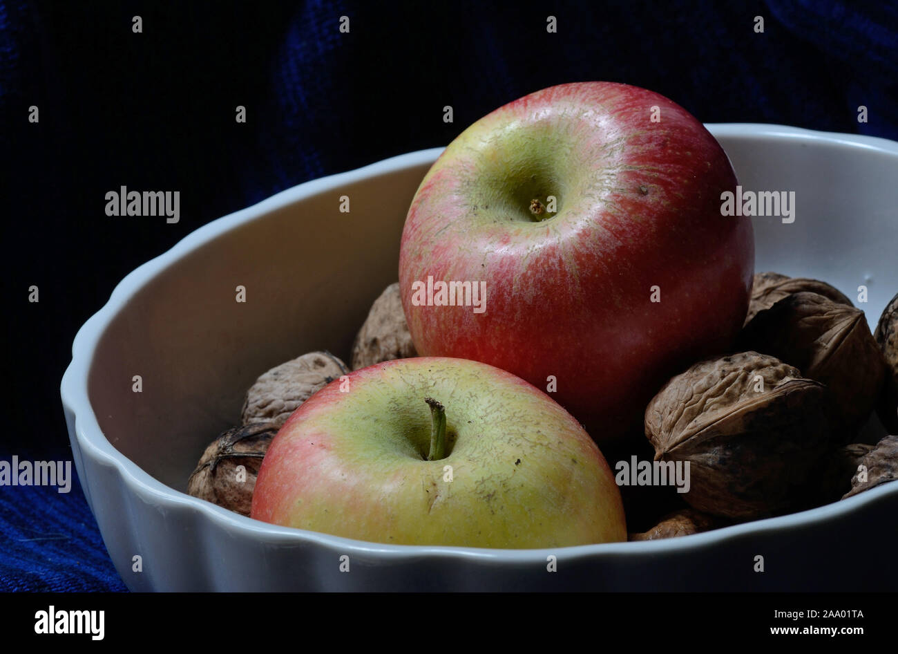 red and yellow kanzi apple with whole walnuts in a white fruit bowl in