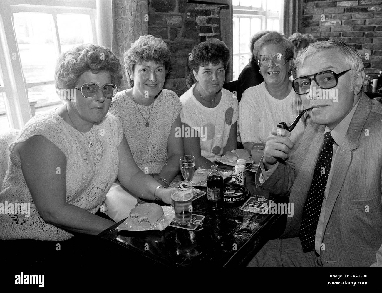 Man smoking his pipe watched by ladies in the pub before the smoking ban Britain, Uk, 1985 Stock Photo
