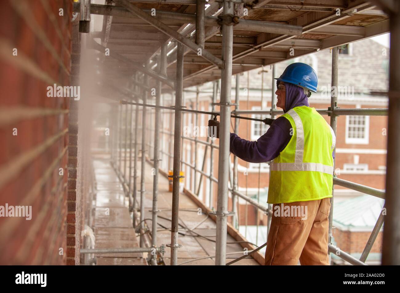 A person wearing safety gear and standing on a scaffold, uses a spray gun while working on the exterior of Gilman Hall, on a cold day at the Johns Hopkins University, Baltimore, Maryland, March 11, 2009. From the Homewood Photography Collection. () Stock Photo