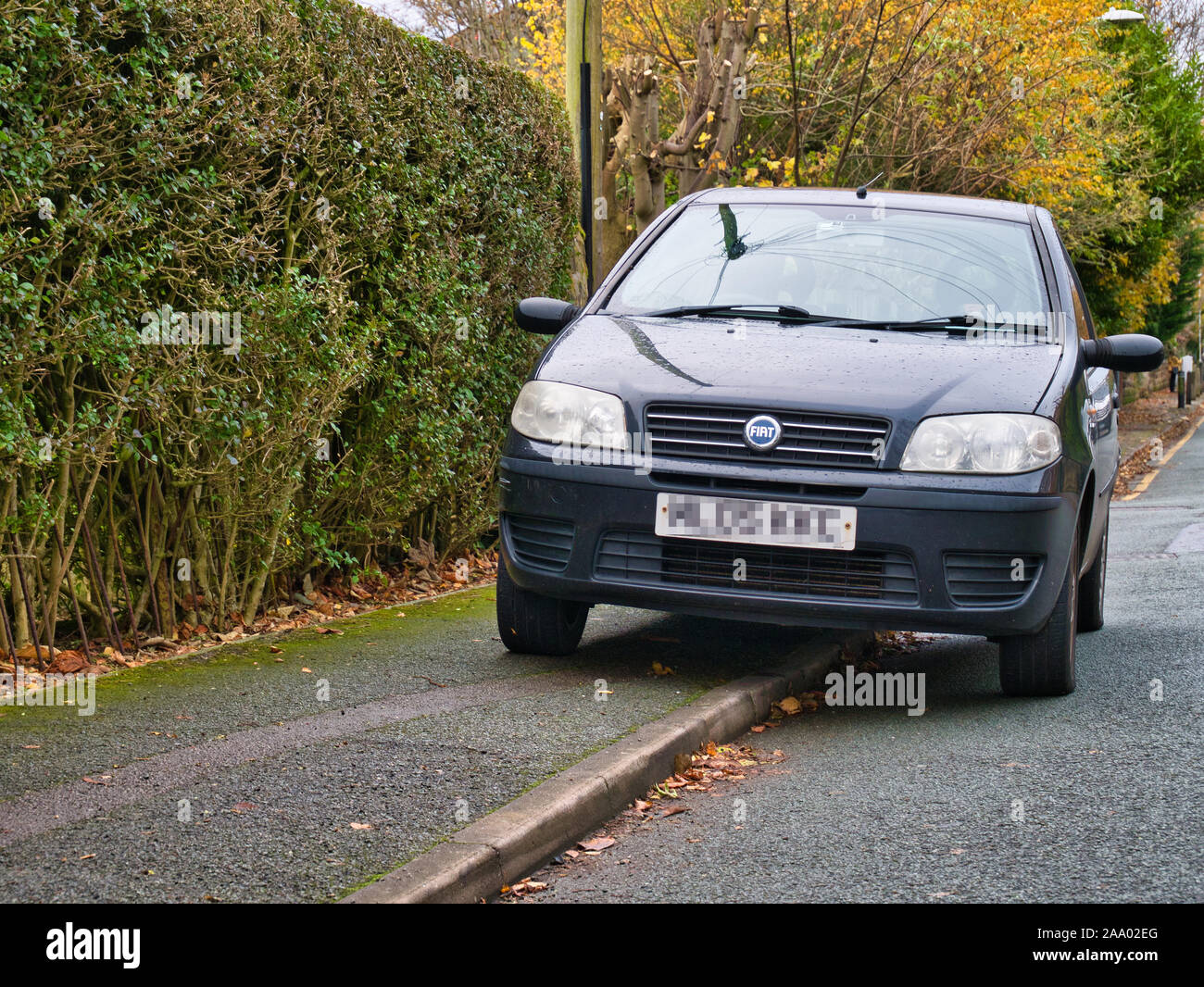 A car parks on the pavement / sidewalk, restricting space for pedestrians - taken in the UK. Stock Photo