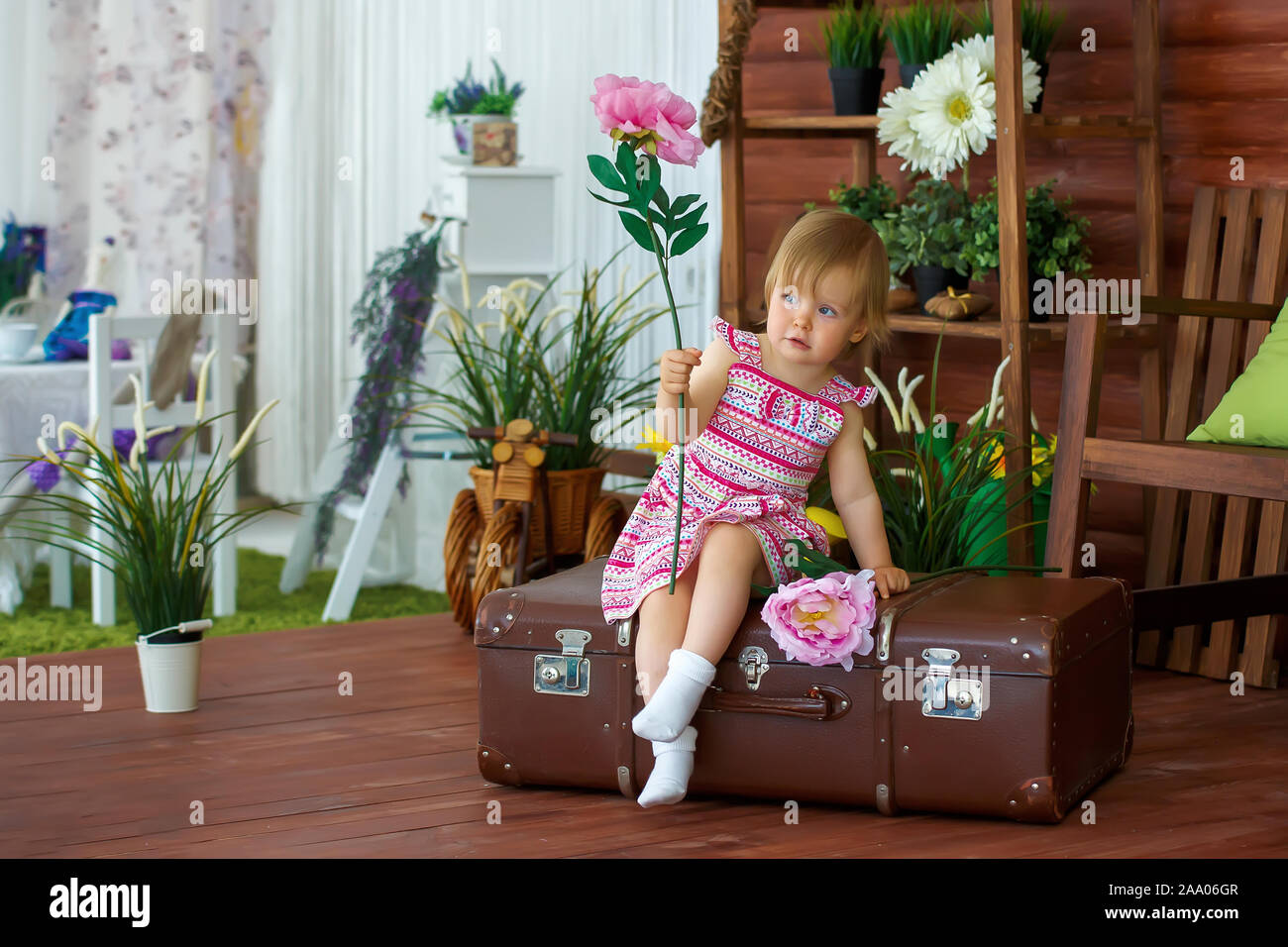 Little girl with a big flower sitting on a suitcase Stock Photo