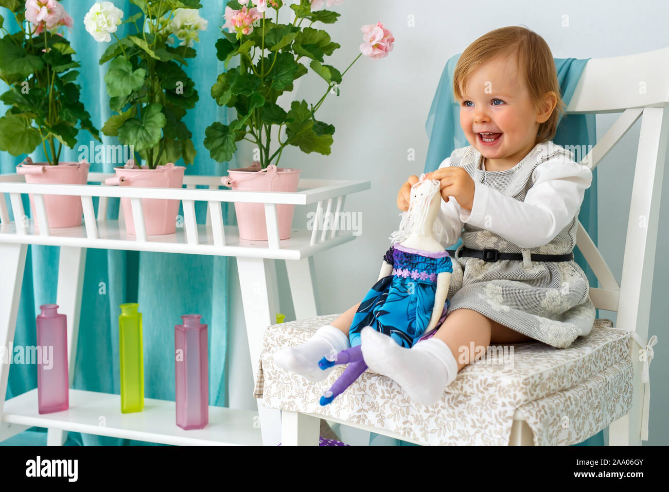The little girl is sitting on a big chair and smiling. Girl holding a doll Stock Photo