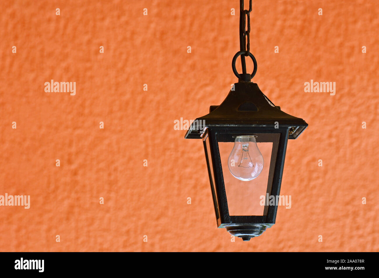 Hanging street lamp in black with an incandescent lamp on the background of the orange wall. Stock Photo