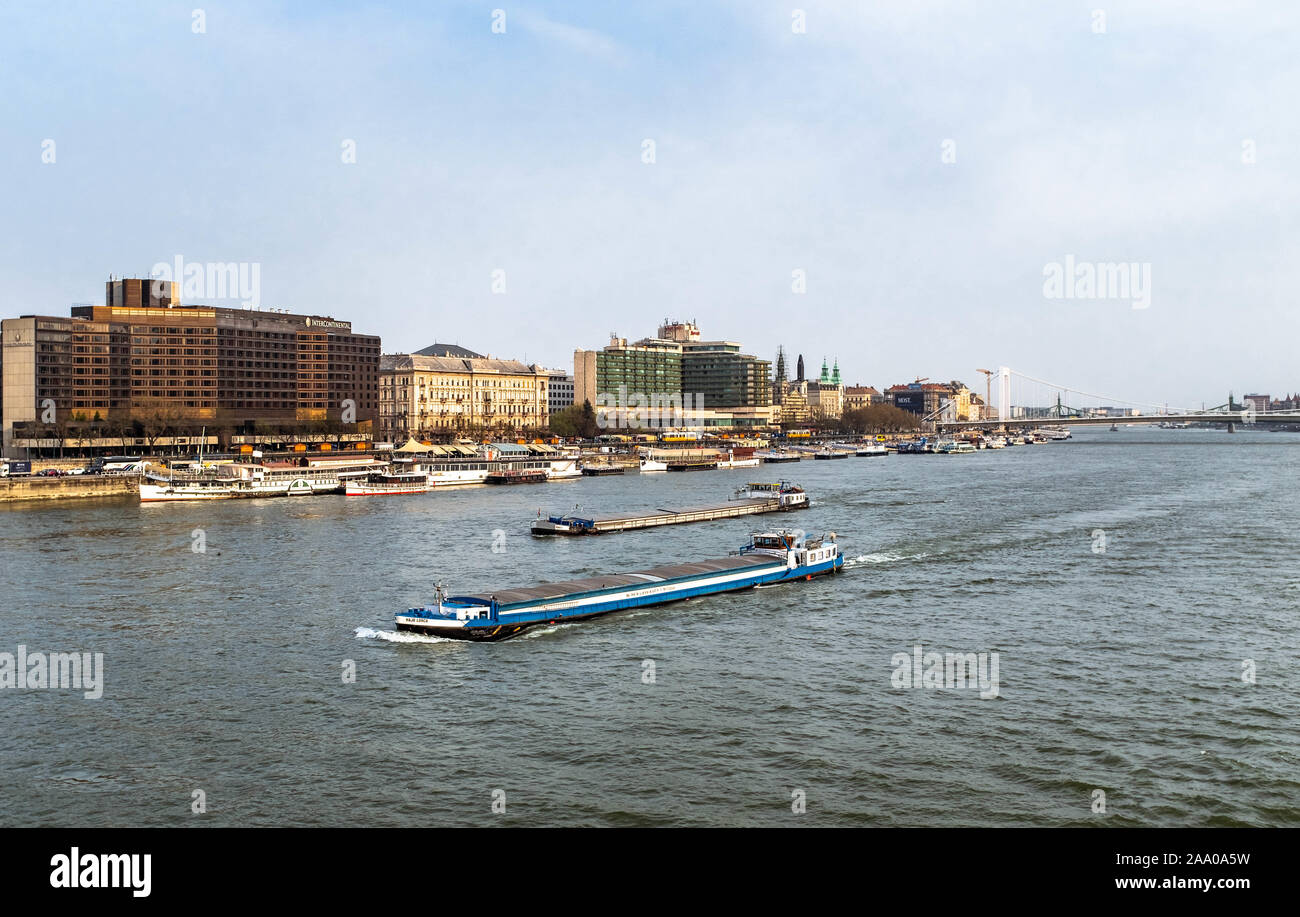 Two river cargo ships sailing in Danube with city scene on background on a sunny spring day. Stock Photo