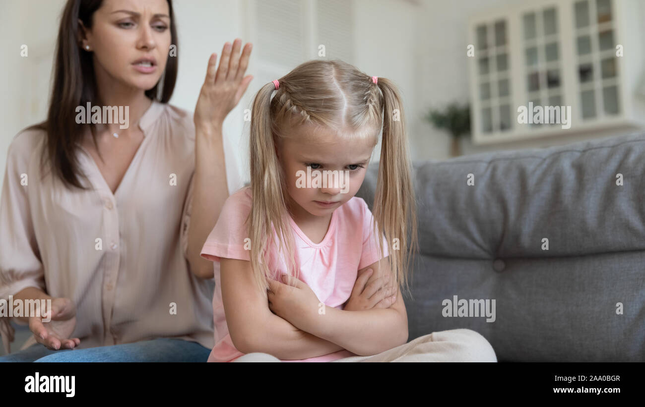 Abused kid girl sitting on couch back to moralizing mother. Stock Photo