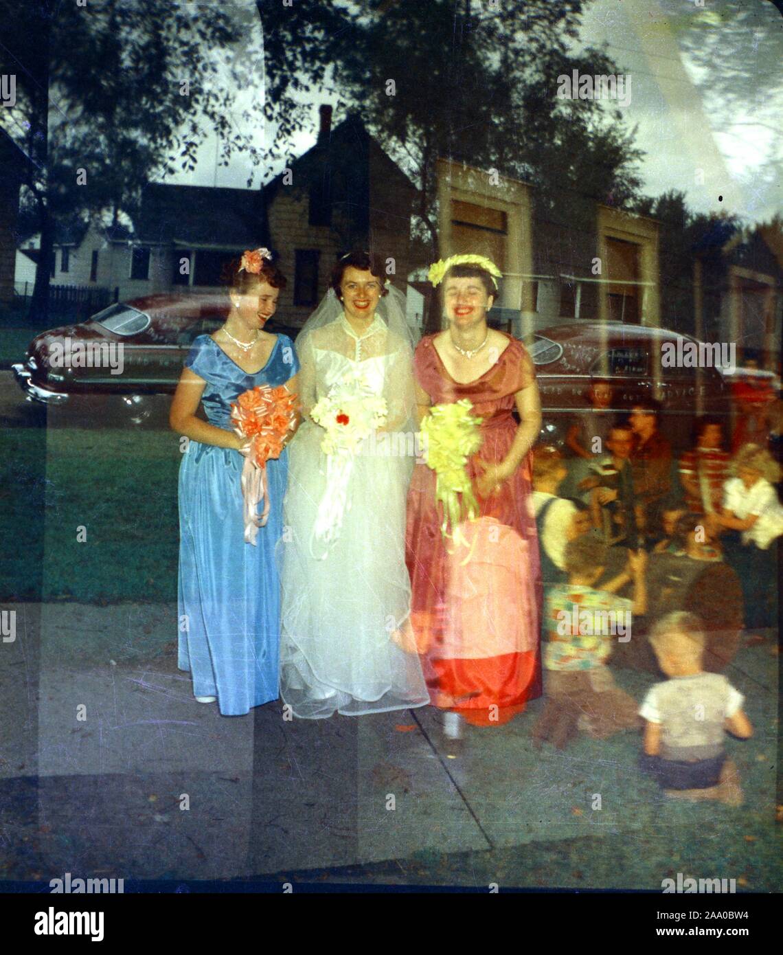 Vintage example of a photographic triple exposure, where a negative is accidentally exposed three times, showing a wedding party with bride and two bridesmaids, a church, and children playing indoors during a party, 1955. () Stock Photo