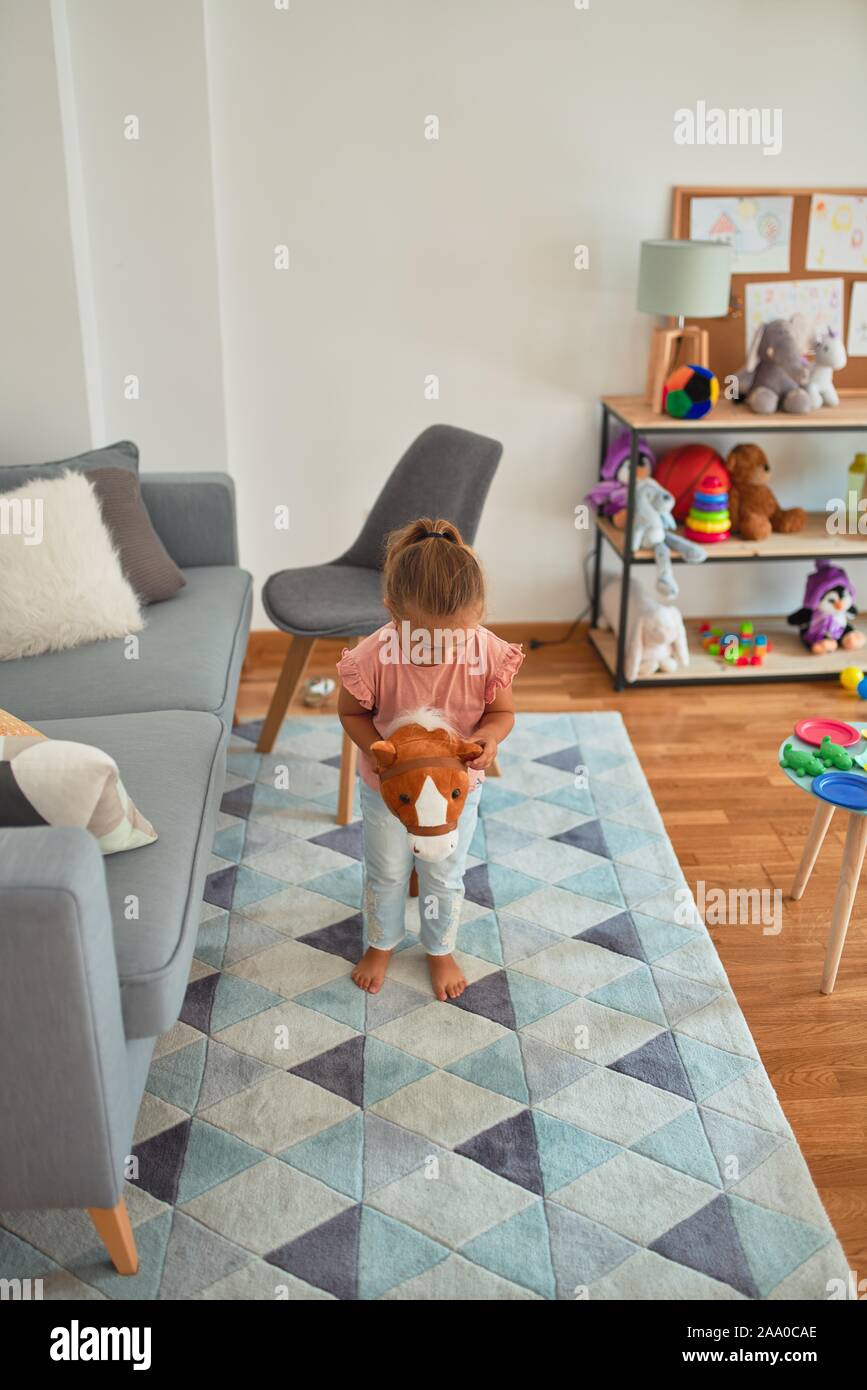 Beautiful blond toddler girl ridding horse with stick toy at kindergarten Stock Photo