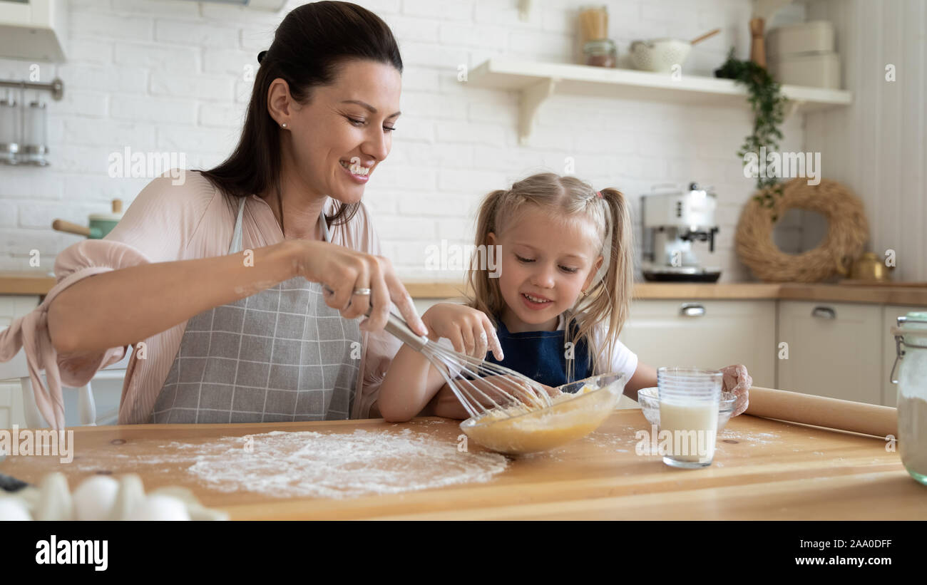 Little child girl in flour watching young mommy stirring eggs Stock