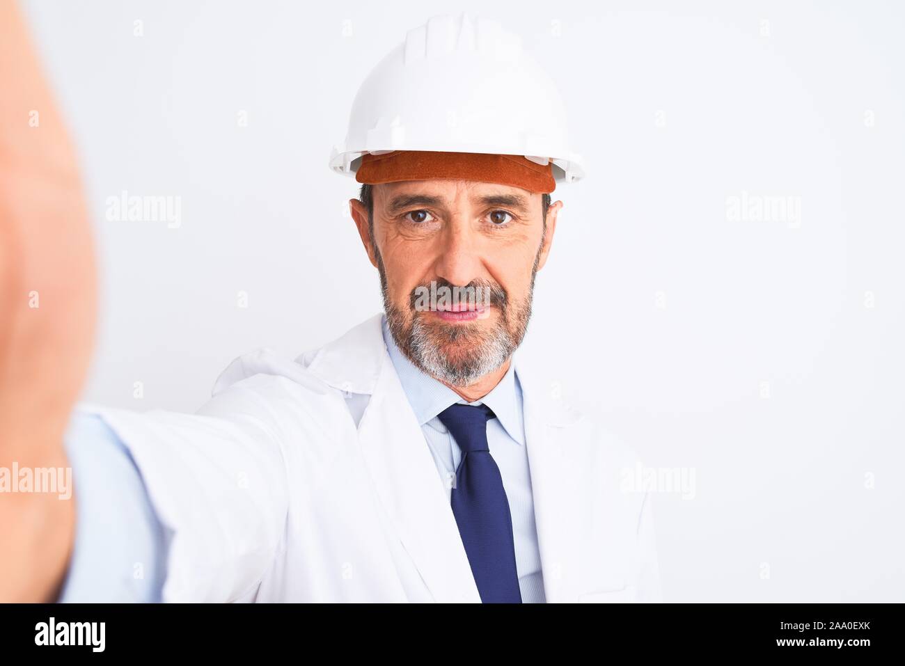 Middle age engineer man wearing helmet make selfie over isolated white ...