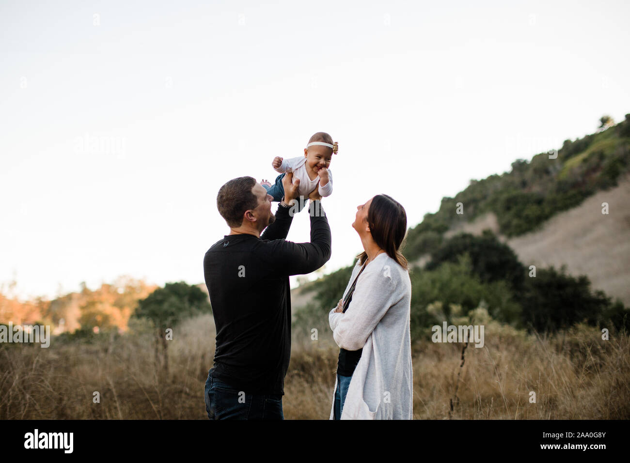 Dad Lifting Infant Daughter as Mom Watches and Smiles Stock Photo