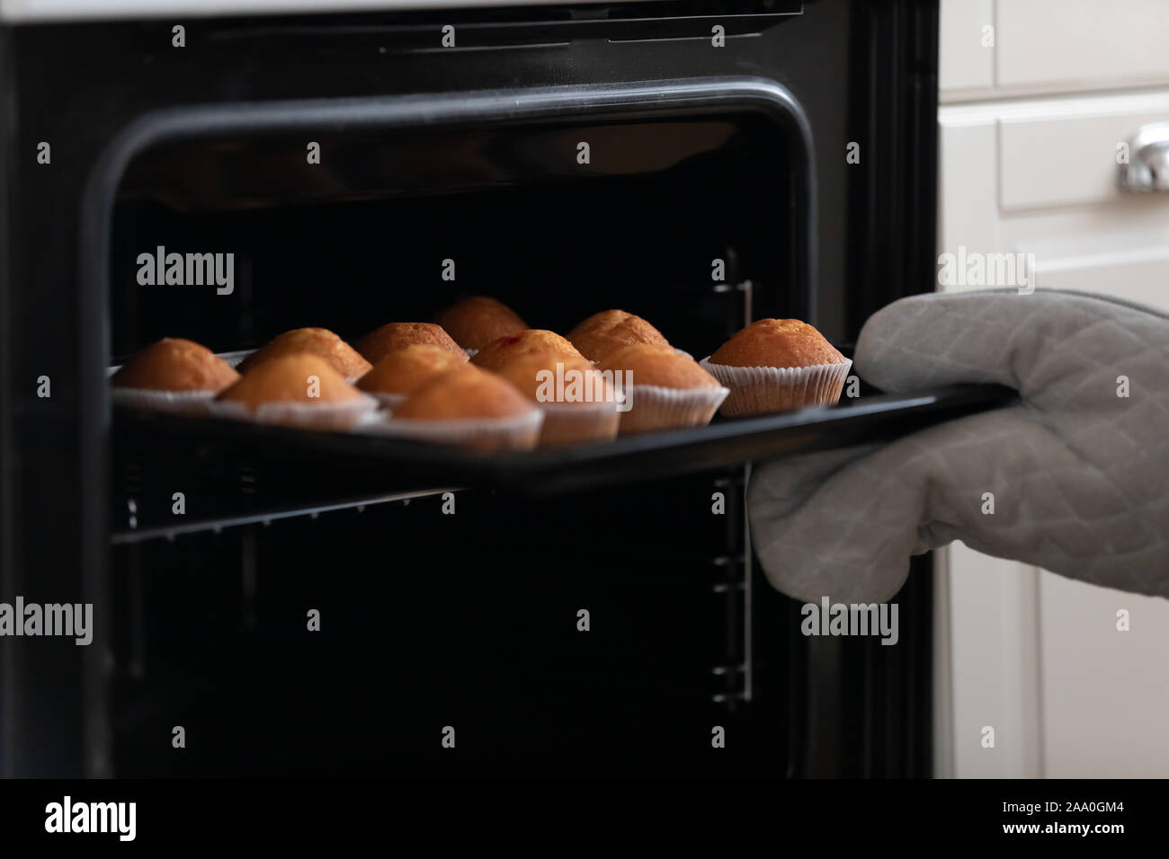 Housewife or professional confectioner taking appetizing muffins out of oven. Stock Photo
