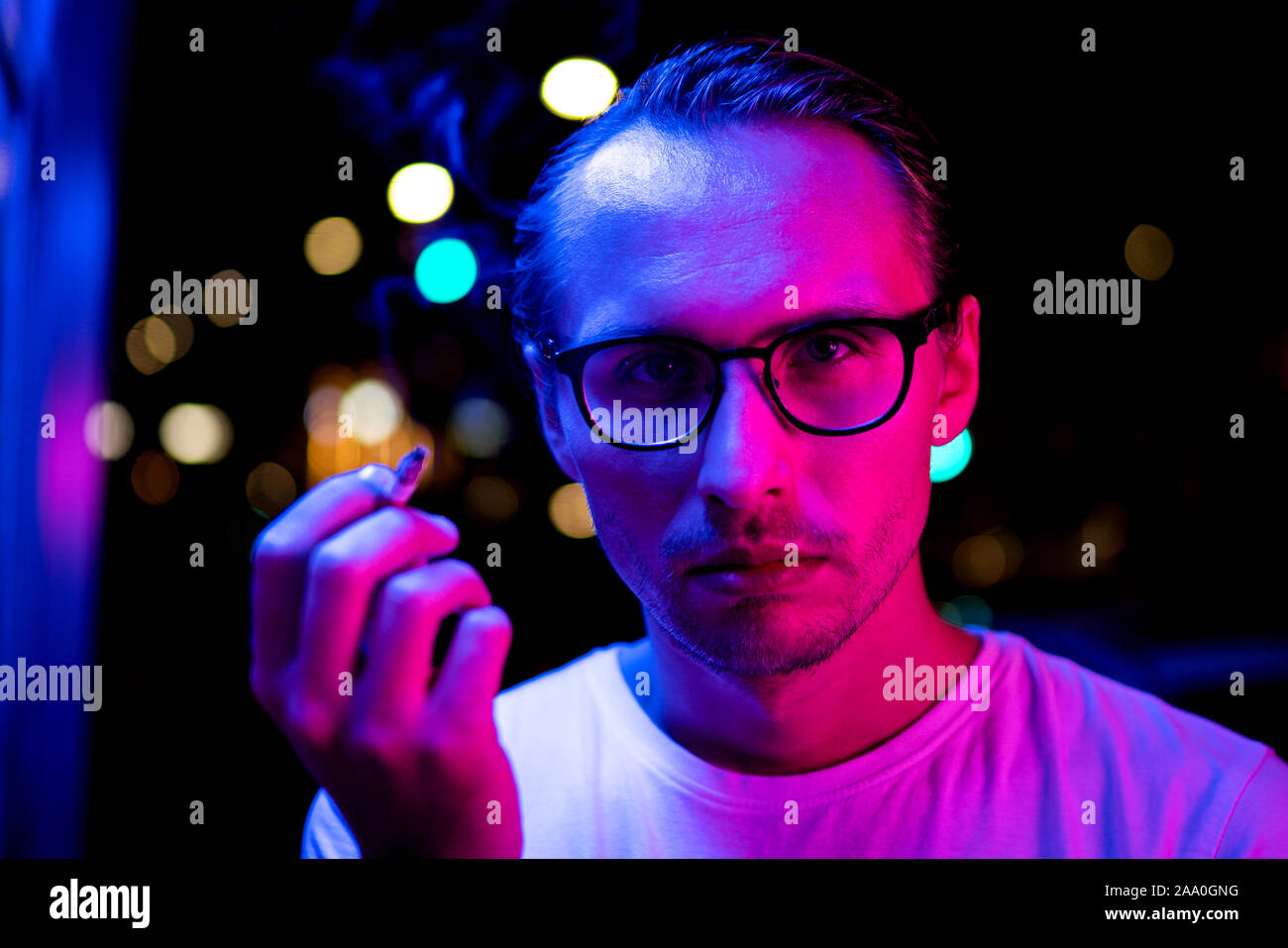 Vintage, red and blue portrait of a young man smoking a cigarette. Street lights visible in the background. Stock Photo