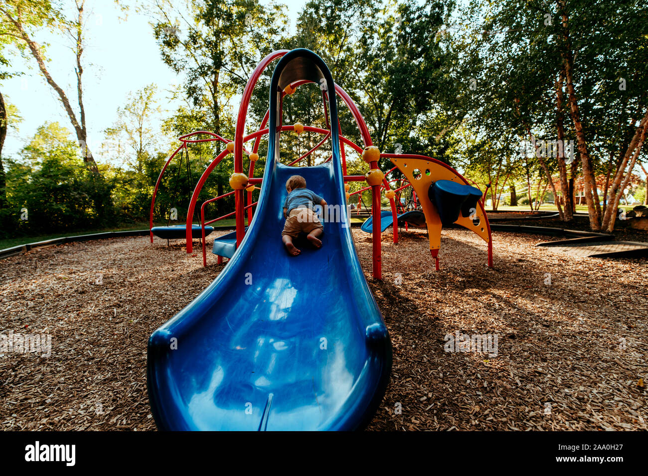 Toddler boy climbing blue slide at park Stock Photo