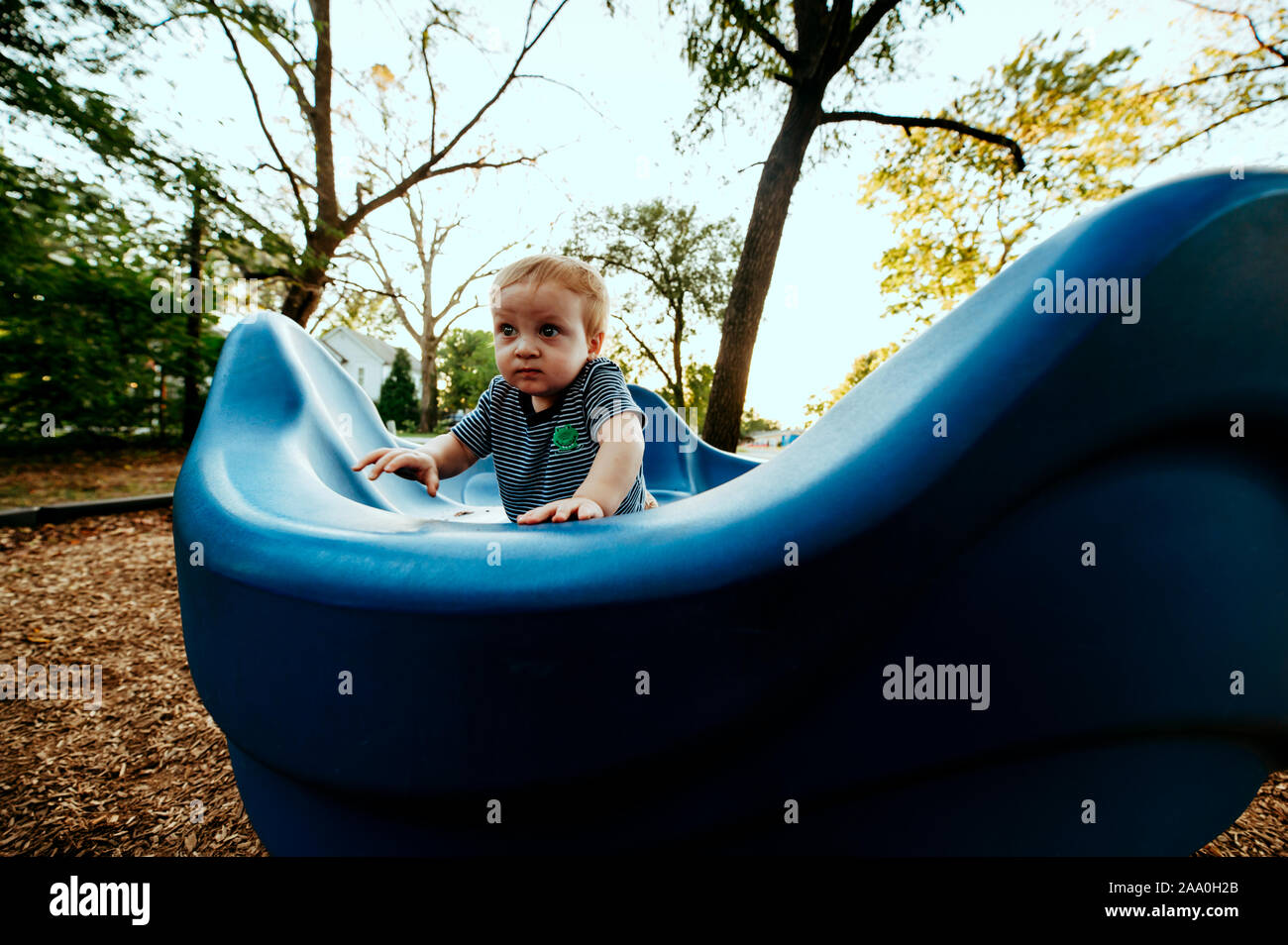 Toddler boy playing on blue playground equipment at park Stock Photo