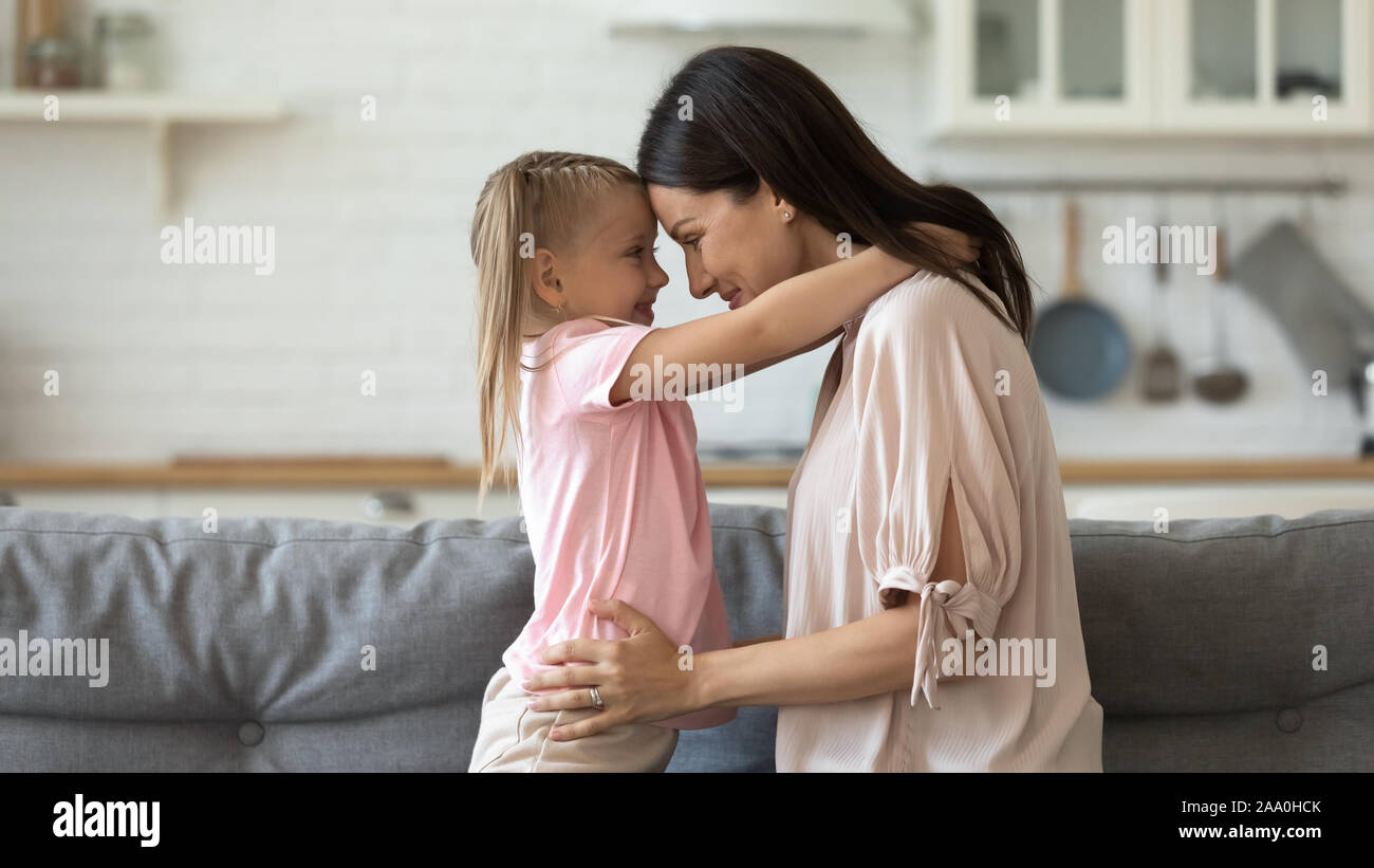 Little preschool girl embracing smiling young mommy, touching foreheads. Stock Photo