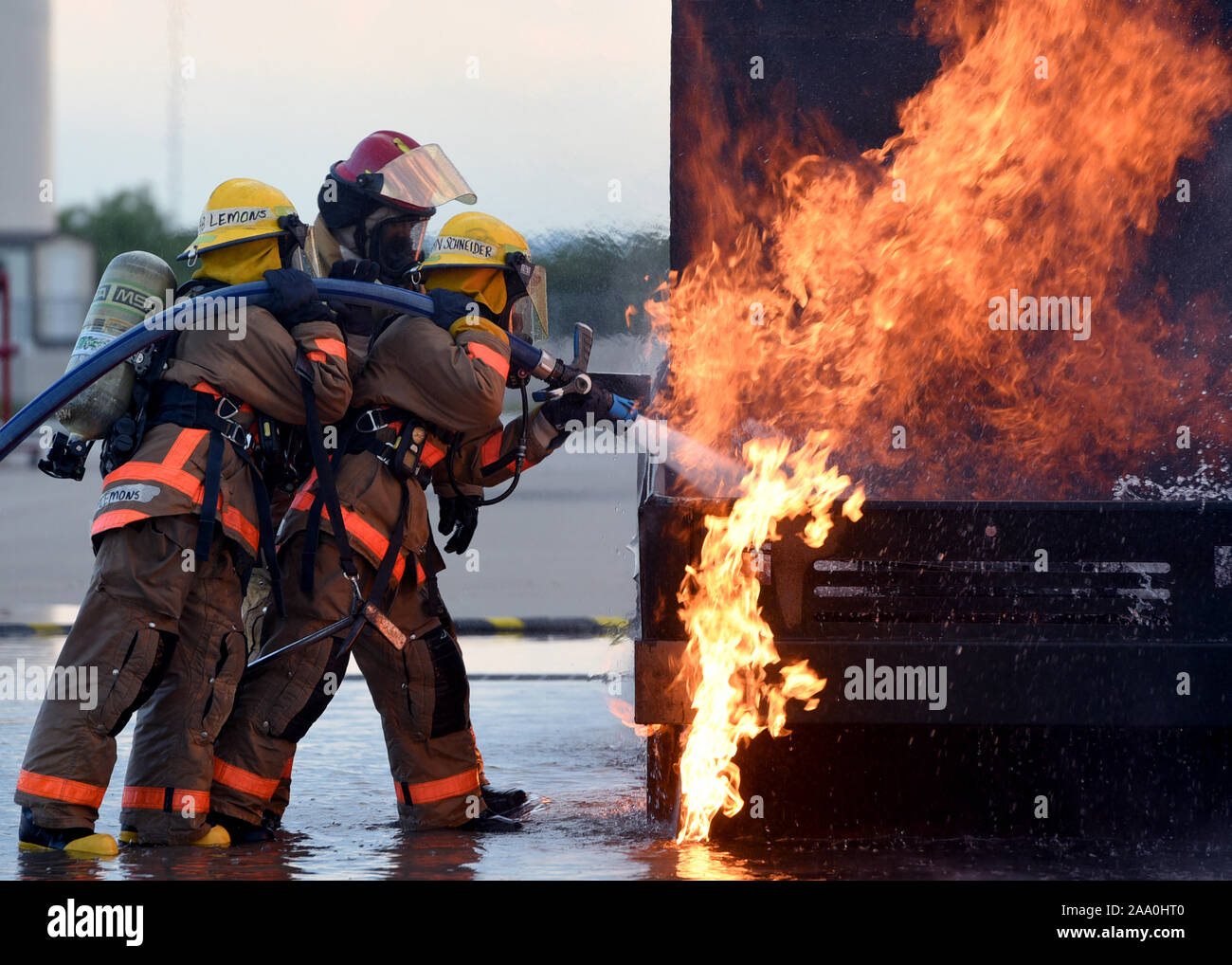 U.S. Air Force Airman Kristina Schneinder, 312th Training Squadron student, leads Airman Emalie Lemons, 312th TRS student, in a textbook style approach to a mock vehicle fire outside the Louis F. Garland Department of Defense Fire Academy on Goodfellow Air Force Base, Texas, July 11, 2019.  Schneinder and Lemons were trained in the classroom how to approach a live fire and what angle to spray the water hose for hood and undercarriage fires before their hands on experience. Stock Photo