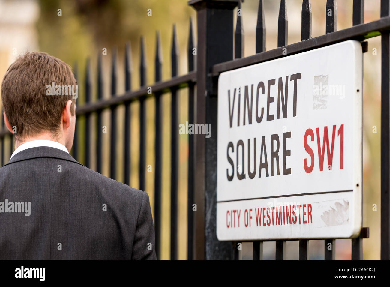 A man walking with the metal fence with street sign which surrounds the playing field and sports ground in Vincent Square City of Westminster, London. Stock Photo
