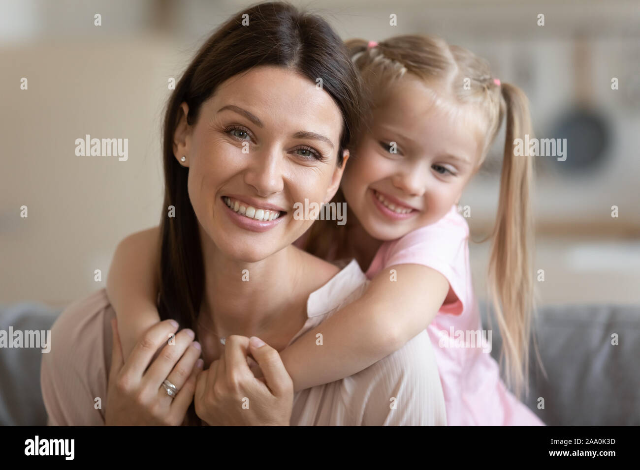 Smiling preschool girl cuddling from back happy young mother. Stock Photo