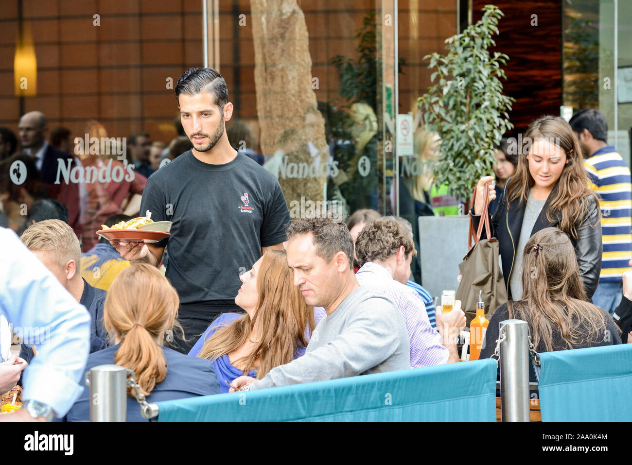 A waiter delivers food to a busy Nando's restaurant terrace in The City of Westminster, London Stock Photo