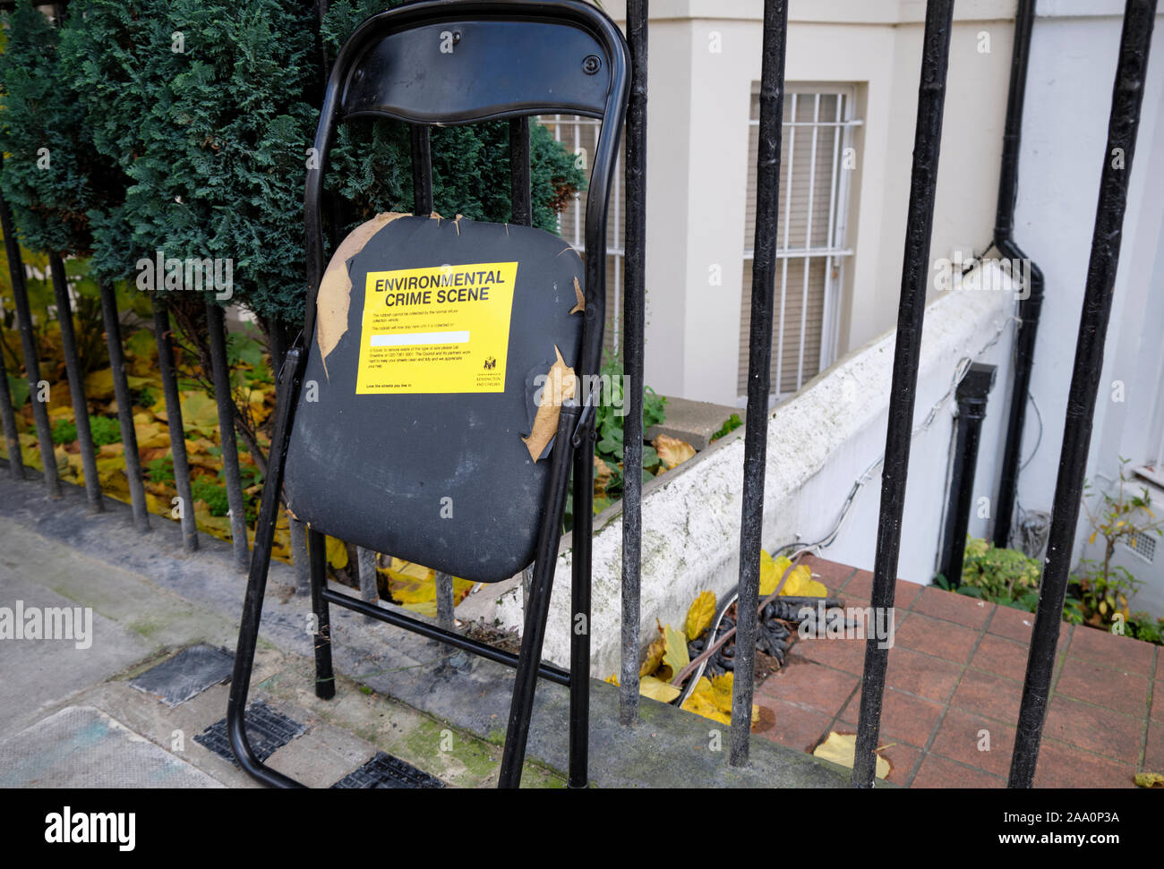 Rubbish broken chair left uncollected on sidewalk with yellow label 'Environmental crime scene' from borough of Kensington and Chelsea, Stock Photo