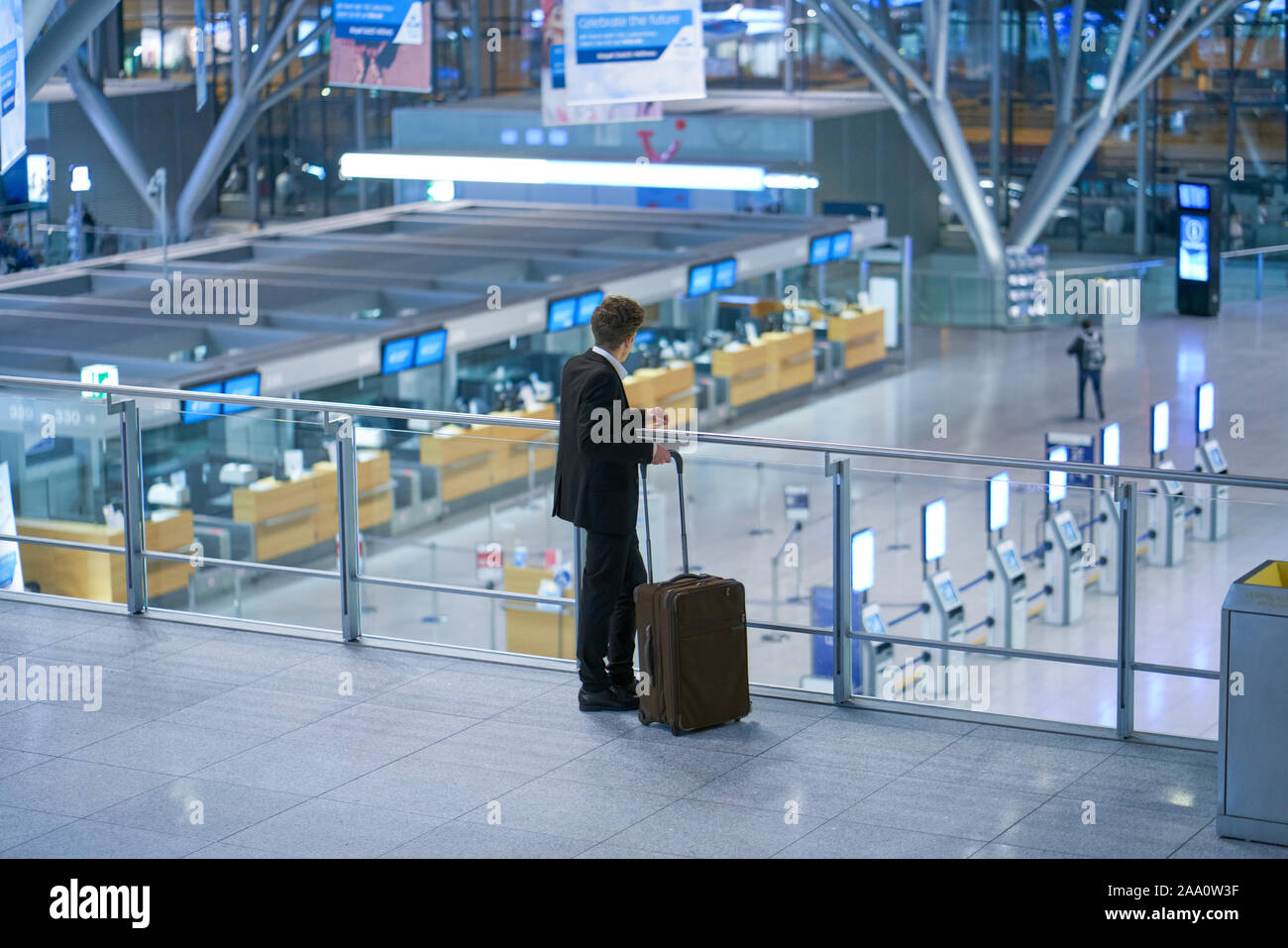 Back of young businessman standing inside the airport with his baggage looking down on the departure lounge Stock Photo