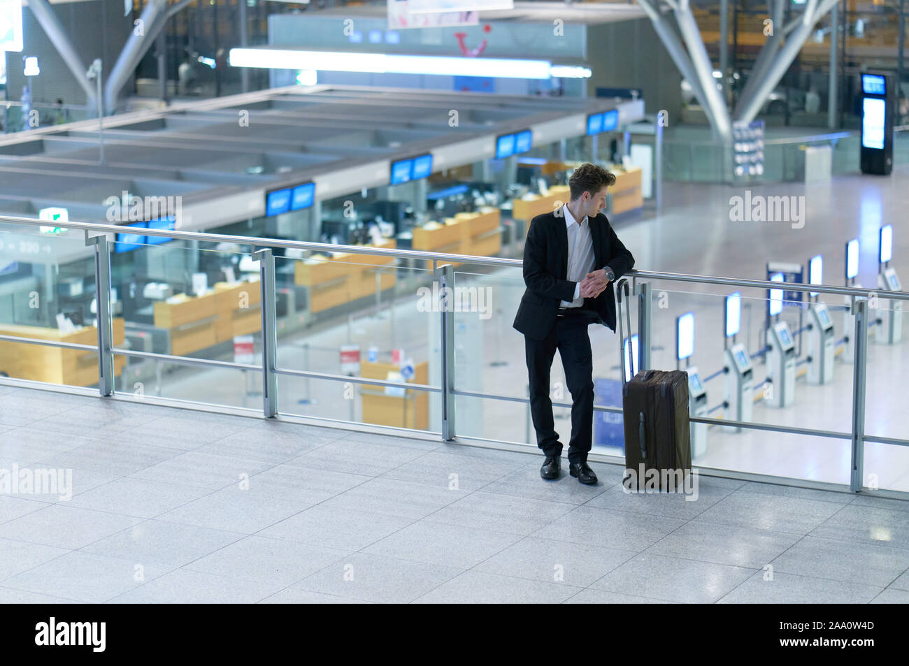 Front of young businessman standing inside the airport looking down on the departure lounge, leaning at the guard railing Stock Photo