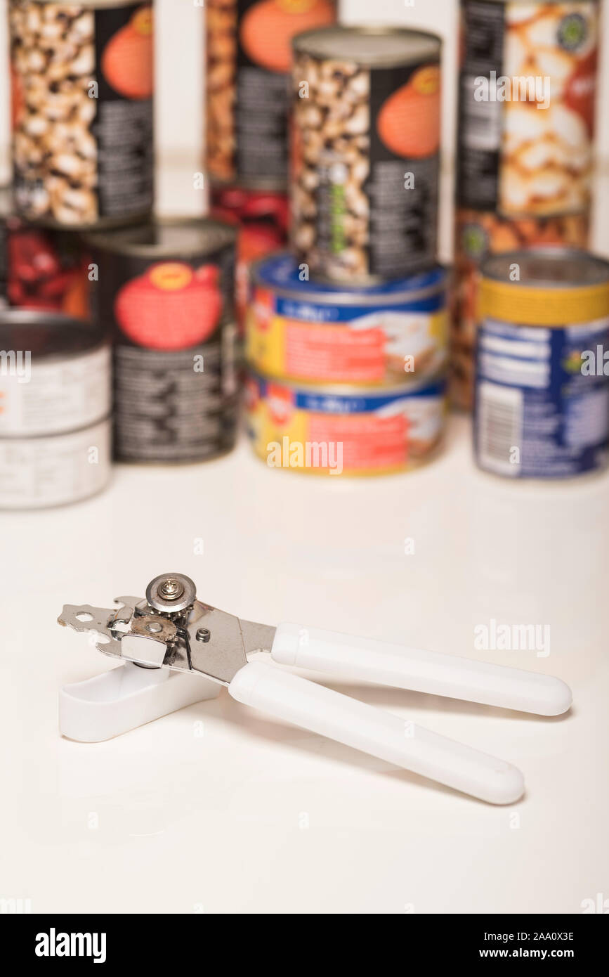 A tin / can opener in front of a background of tinned / canned foods
