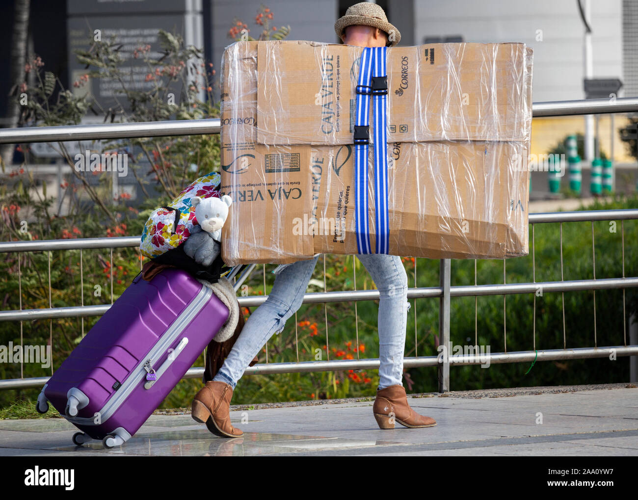 Woman with wheeled suitcase carrying large packet, parcel. Stock Photo