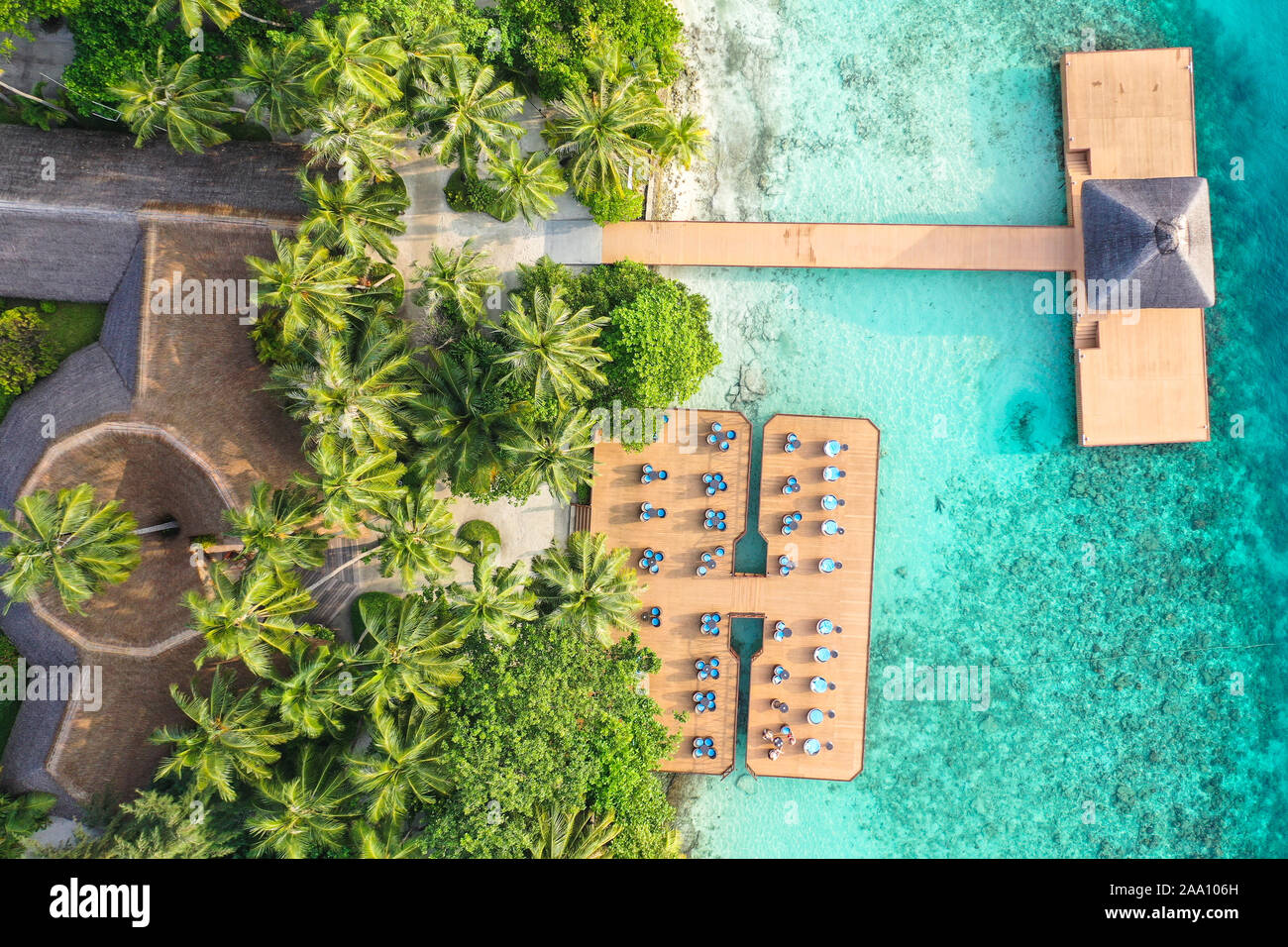 Aerial top down view from drone of a luxurious tropical island paradise resort in Maldives with wooden pier and relaxing area with chairs and tables Stock Photo