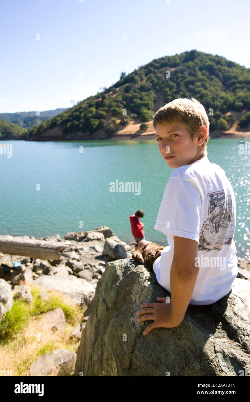 Portrait of a boy sitting on a rock near a lake Stock Photo - Alamy