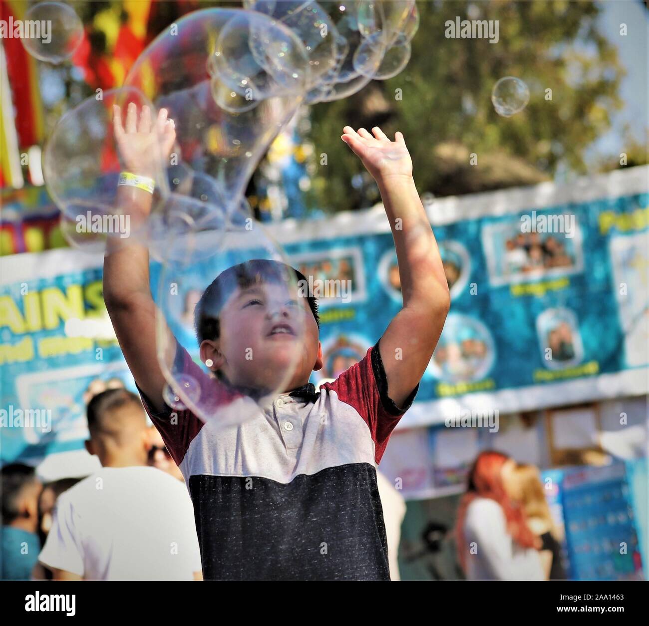 Hispanic Latin Mexican kids, boys and girls, chasing bubbles from fair circus act made with soap and water for public entertainment and family fun Stock Photo