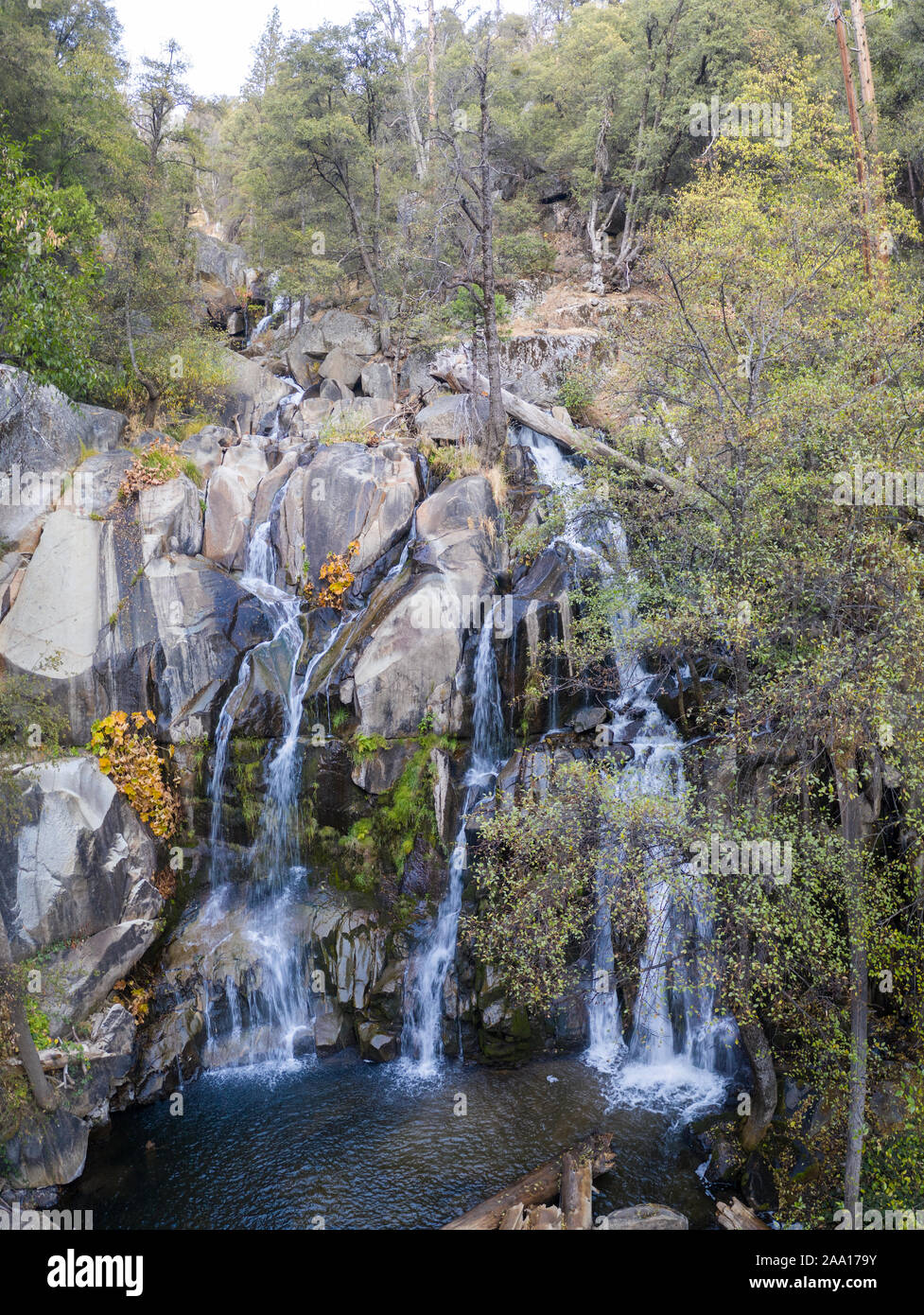 Freshwater from a stream tumbles down a rocky cliff face forming a beautiful waterfall in a wild California forest. Stock Photo