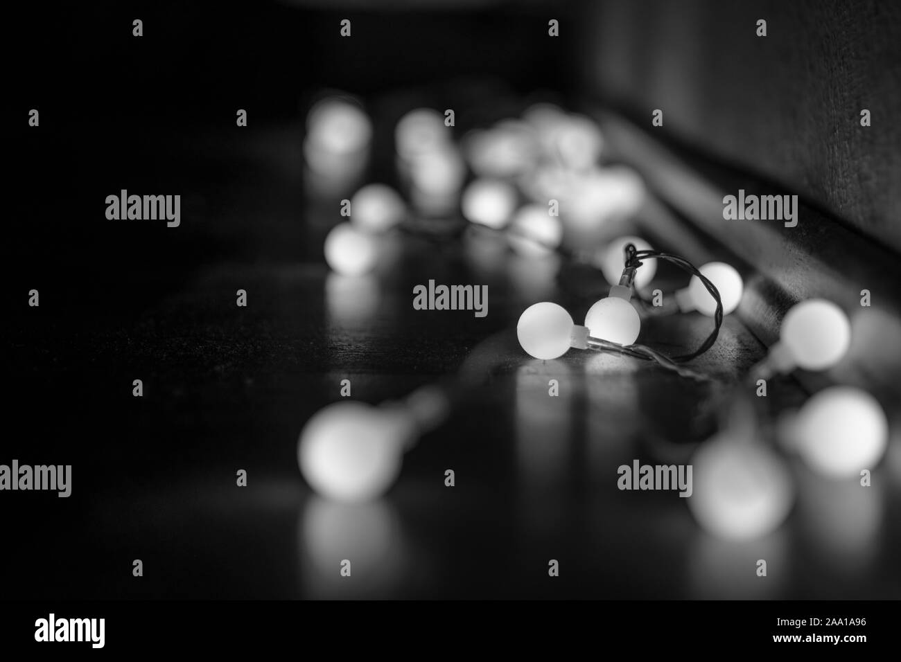 Black and white mood and tone of close up view of decorative wire led small warm white light bulbs lay on a floor at corner of dark and dim room. Stock Photo