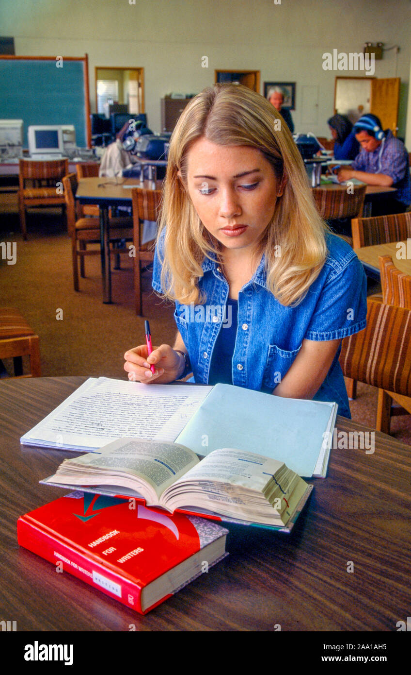 Aided by a grammar textbook, a female community college student negotiates a writing assignment in the college library in Long Beach, CA. MODEL RELEASE Stock Photo