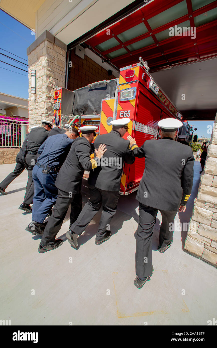 Formally uniformed firemen push a fire engine into a new fire station as part of the station's ritualistic dedication ceremony in Newport Beach, CA. Stock Photo