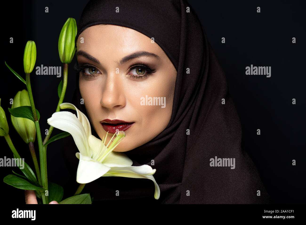 attractive Muslim woman in hijab with red lips holding lily isolated on ...