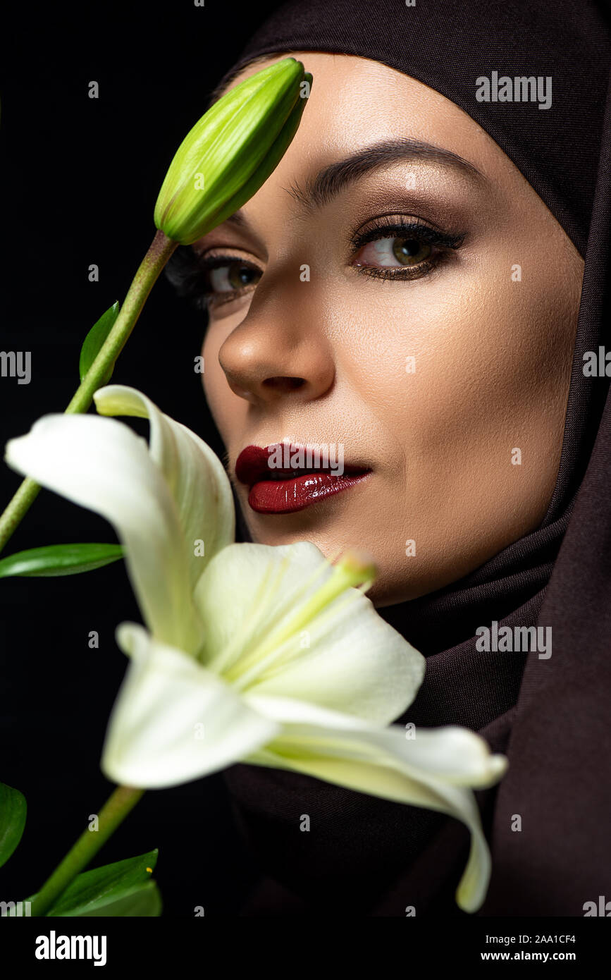 portrait of attractive Muslim woman in hijab with red lips holding lily ...