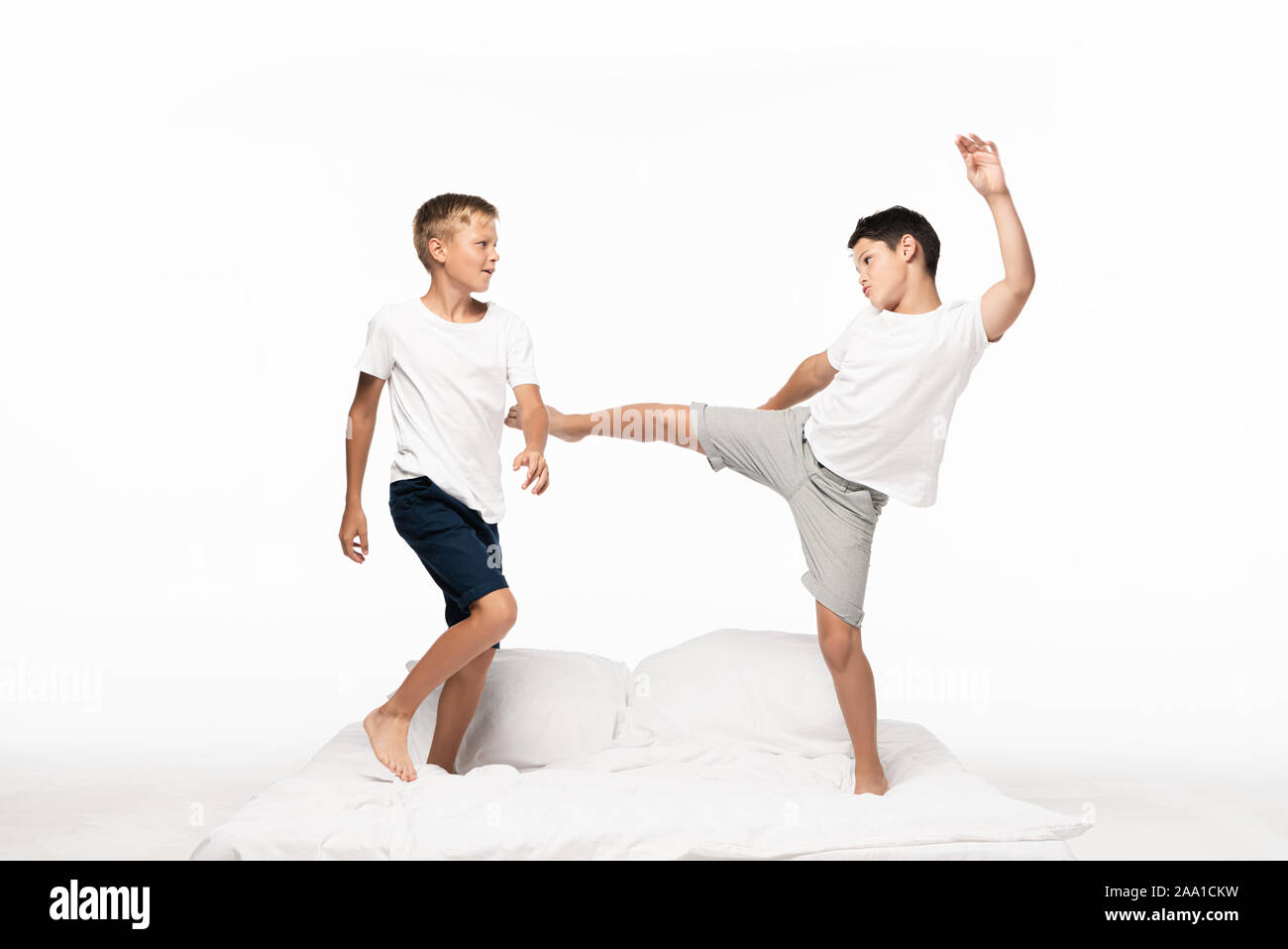 boy jokingly kicking brother with leg while having fun on bed isolated
