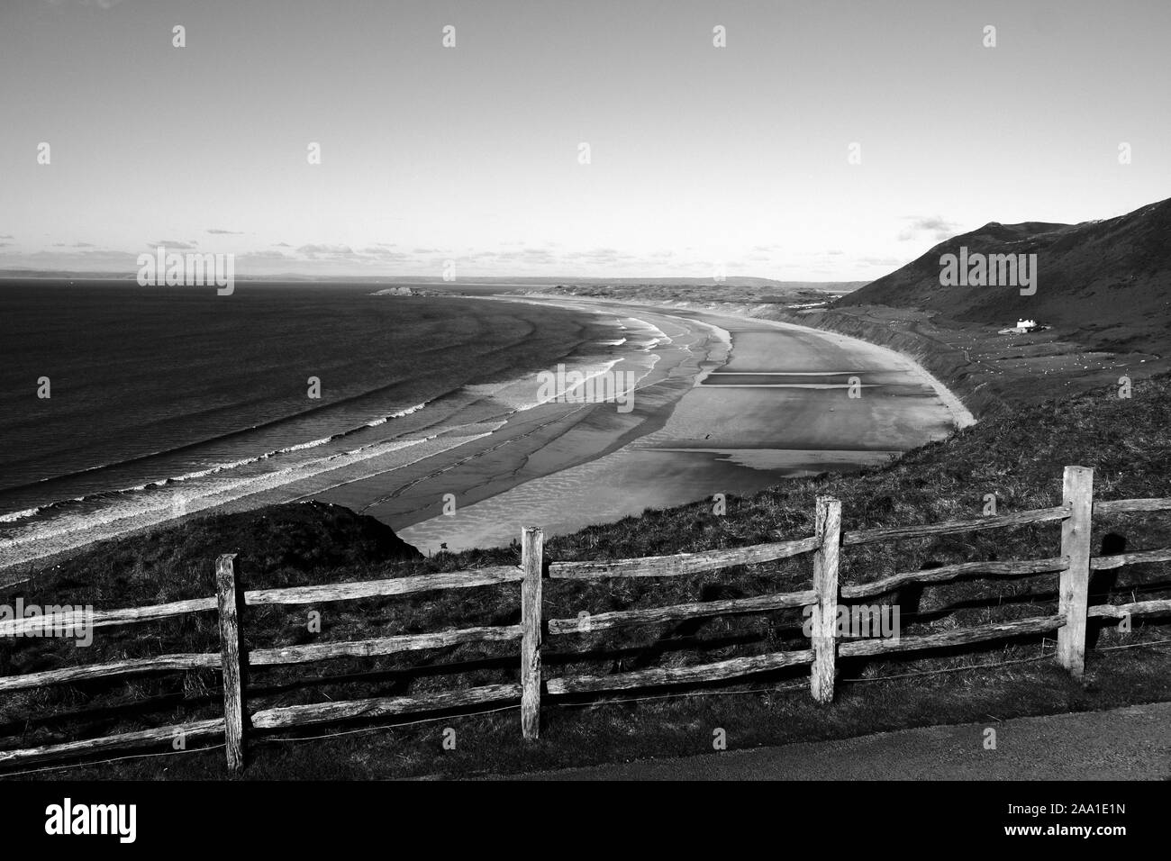 View of Rhossili Bay from the National Trust carpark above with a wooden stock fence in front of the sheep grazing pasture land on the hillside Stock Photo