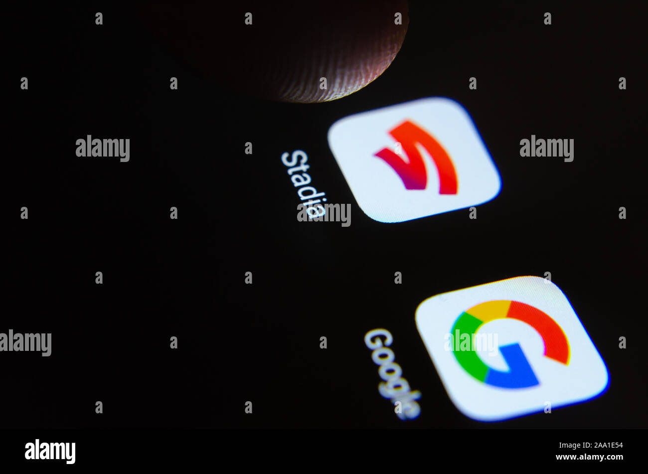 Stadia and Google apps on a smartphone screen and finger launching Stadia. Stock Photo