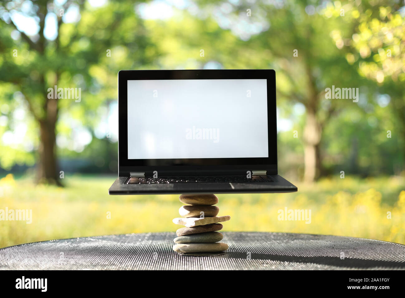 Laptop with blank screen outdoors balancing on stones surrounded by ...