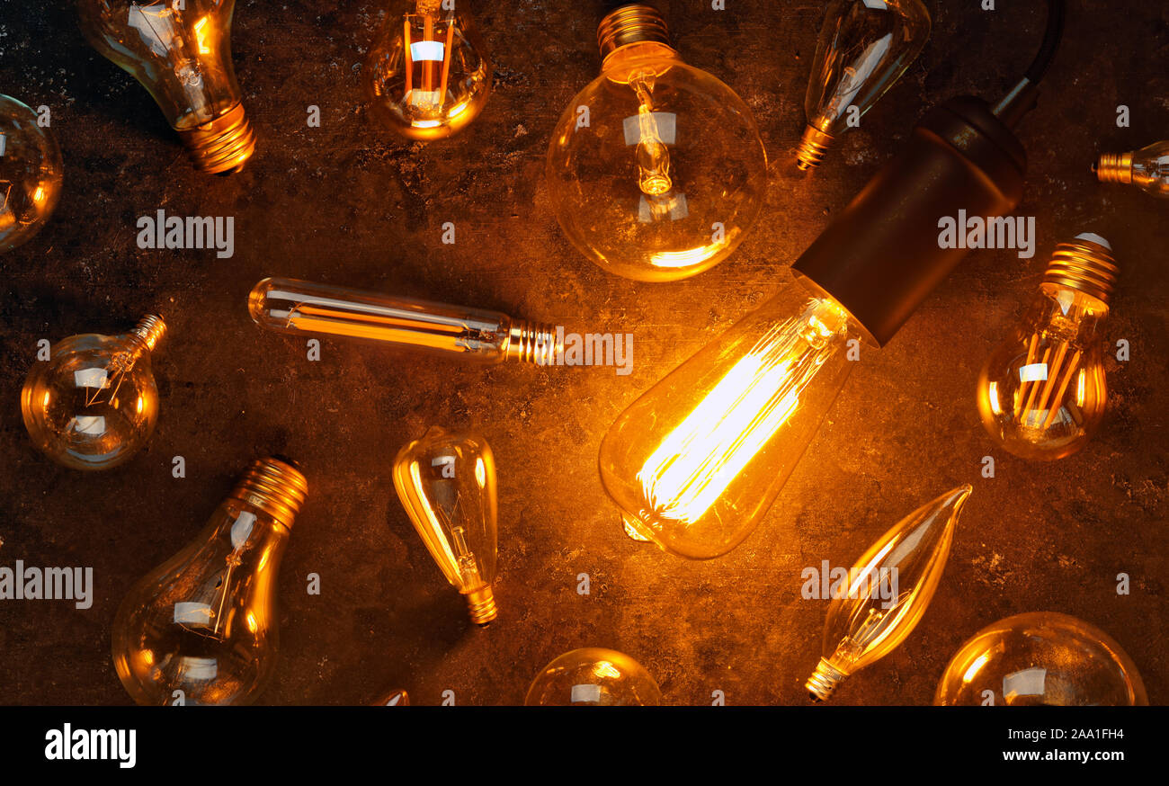 Vintage old light bulb glowing yellow on rough dark background surrounded by burnt out bulbs. Idea, creativity concept. Stock Photo