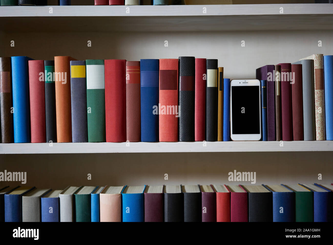Accurate bookcase with mobile phone standing between colorful book covers Stock Photo